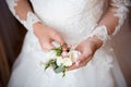 Close up of bride`s hands holding groom`s boutonniere. Woman in a beautiful white dress. Bride`s preparations. Wedding