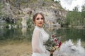 close up. The bride in a white dress with a red bouquet on the bank of a river . Royalty Free Stock Photo