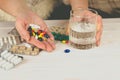 Close-up of bright colored medical pills and capsules with medicines in a woman`s hand and a glass of water next to them. Medicin Royalty Free Stock Photo