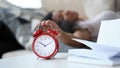 Close-up of bright red alarm clock and young latino woman turning it off while laying in bed Royalty Free Stock Photo