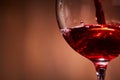 Close-up of brightly red wine poured in the wineglass and abstract splashing against brown background. Royalty Free Stock Photo