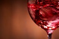 Close-up of brightly red wine poured in the wineglass and abstract splashing against brown background. Royalty Free Stock Photo