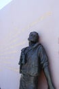 A bronze sailor sculpture leaning against an engraved wall of the USS San Diego Memorial in San Diego, California