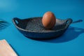 Close-up of a brown egg with a fork in the pan against a blue background Royalty Free Stock Photo