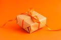 Close up of brown gift box with a orange satin ribbon bow on orange blurred background with copy space. Holiday autumn concept Royalty Free Stock Photo