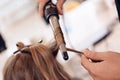 Close up. Brown hair woman does curling hair in beauty salon. Hairdresser make hair wave for woman.