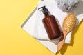 Close-up of a brown shampoo bottle, a detangling comb, a towel and a bath sponge placed on a tray against a yellow background. Royalty Free Stock Photo