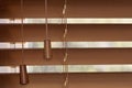 A close up of brown Venetian blinds partly opened with chords on one side