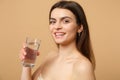 Close up brunette half naked woman 20s with perfect skin nude make up glass water isolated on beige pastel wall Royalty Free Stock Photo