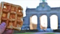 Close up of a Brussels Gaufre. In the background, the fiftieth anniversary building.