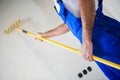 Close up, a builder in blue uniform paints a wall in white with a roller