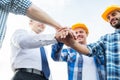 Close up of builders in hardhats with hands on top