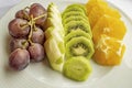 Bunch of grapes, sliced kiwi, apple and orange fruits in white plate Royalty Free Stock Photo