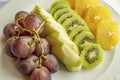 Bunch of grapes, sliced kiwi, apple and orange fruits in white plate Royalty Free Stock Photo