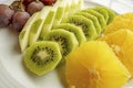 Bunch of grapes, sliced kiwi, apple and orange fruits in white plate Royalty Free Stock Photo