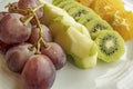 Bunch of grapes, sliced kiwi, apple and orange fruits in white plate Royalty Free Stock Photo