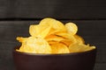 Close-up of a bunch of potato chips in a brown plate on a dark wood