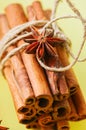 Close up of bundle of cinnamon sticks and anise stars over yellow background.