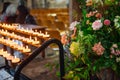 Close up burning candles in sconces on background of flowers and catholic cathedral interior. Selective focus, copy space. Royalty Free Stock Photo