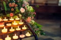 Close up burning candles in sconces on background of flowers and catholic cathedral interior. Selective focus, copy space. Royalty Free Stock Photo