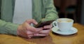 Close up of businessman at cafe sitting on a table reading phone message or downloading an app for his mobile phone.