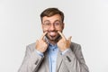 Close-up of businessman in gray suit and glasses trying to pull a happy smile, standing over white background