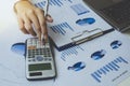 Close up of businessman hand holding pen while using calculator to calculate data on graph chart paper. Accountancy documents and