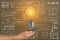 Close up of businessman hand holding smartphone with glowing light bulb on chalkboard wall background with mathematical formulas. Royalty Free Stock Photo