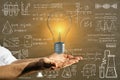 Close up of businessman hands holding glowing light bulb on chalkboard wall background with mathematical formulas. Science, idea Royalty Free Stock Photo