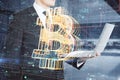 Close up of businessman hands holding laptop with creative glowing bitcoin hologram on blurry office interior background.