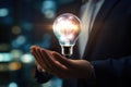 Close up of businessman holding light bulb in palm with cityscape at background, Businessman, set against a blurred background, Royalty Free Stock Photo