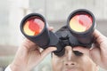 Close up of businessman looking through binoculars, red reflection in the glass