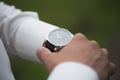 Close up of businessman looking at watch on his hand outdoors, free space. Man in white shirt checking time from luxury