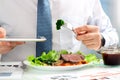 Close-up of businessman working on marketing strategy during business lunch, eating juicy club steak.