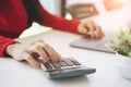 Close-up of a businesswoman hands using laptop and counting on calculator.