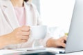 Close up of businesswoman using laptop computer and sitting at office desk, holding a cup of coffee Royalty Free Stock Photo