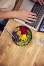 Close Up Businesswoman Working On Laptop Whilst Eating Vegan Lunch At Wooden Table