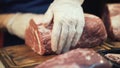 Close-up of butcher hands in white protective gloves preparing a large cut of meat for cooking or sale. Action. Butcher