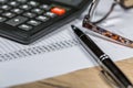 Calculator, pen, glasses and business document lie on the surface of a wooden table Royalty Free Stock Photo