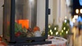 Close-up of candle in glass candlestick on background of festive decorations. Action. Glass outdoor candle holder with
