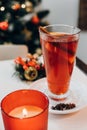 Close-up of candle and mulled red wine with aromatic spices and citrus fruits on white table on background decorated Xmas tree. Royalty Free Stock Photo