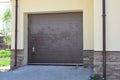 A close-up of a car garage attached to a house with a brown sectional garage door, a paved driveway and rain gutters