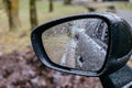 Close up of car side rear view mirror with rain drops on blurred background. Rainy day on the road. Driving in bad Royalty Free Stock Photo