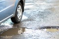 Close up of car wheel on a road in very bad condition with big potholes full of dirty rain water pools Royalty Free Stock Photo