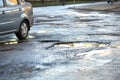 Close up of car wheel on a road in very bad condition with big potholes full of dirty rain water pools Royalty Free Stock Photo