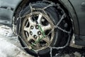 Close-up of a car wheel with snow chains. Dirty rims. Rubber in the snow. Car wheel with chains. Safety on winter snowy