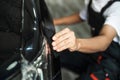 Close-up of car wrapping specialist hand straightening wrapping transparent film for protection with a squeegee.