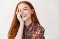 Close-up of carefree female model with ginger hair and blue eyes, covering half of face and laughing with happy face at Royalty Free Stock Photo