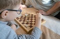 Close-up of a caring middle-aged grandmother playing checkers with a child, a boy, while lying on the bed. Happy family Royalty Free Stock Photo