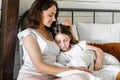 Close up of caring mother hugging tired daughter lying on pillow in bed Royalty Free Stock Photo